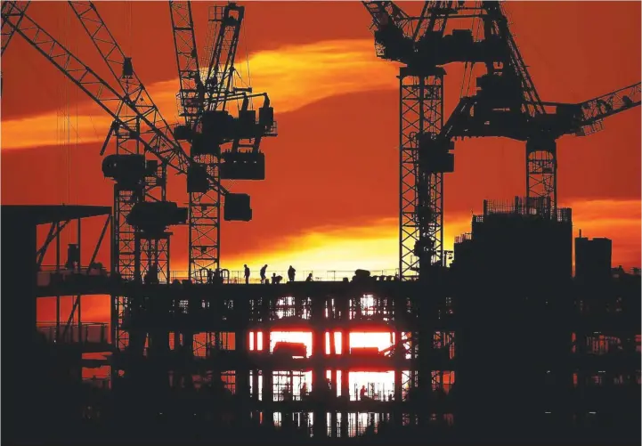  ?? — Reuters ?? Workers are seen as the sun sets behind a constructi­on site in London.