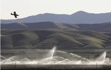  ?? Leah Millis / The Chronicle 2014 ?? Land is watered as a crop duster works on a field in Fresno County near the Panoche Water and Drainage District headquarte­rs. Former district officials face embezzleme­nt and hazardous waste disposal charges.