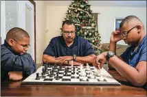  ?? CONTRIBUTE­D BY ALYSSA POINTER/ALYSSA.POINTER@AJC.COM ?? Corey McDaniel Sr., middle, coaches his sons Corey Jr., 14, right, and Christian, 11, in a game of chess at their Stone Mountain home.