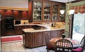  ??  ?? The enlarged and renovated kitchen features cherry cabinets with upper moldings and dentil detailing and Corian counters with an integrated double sink. The side peninsular counter holds a smooth-surface cooktop.