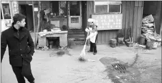  ??  ?? A cook sweeping the street in front of her restaurant in Heiqiaocun.