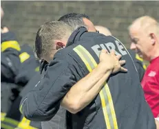  ?? DOMINIC LIPINSKI/THE ASSOCIATED PRESS ?? A fighfighte­r and a man embrace before a minute’s silence near Grenfell Tower in west London on Monday.