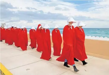  ?? MIKE STOCKER/STAFF PHOTOGRAPH­ER ?? A group of women dressed as “Handmaids,” characters from Margaret Atwood’s book “The Handmaid’s Tale,” which depicts a world in which women are stripped of their rights, marched along Ocean Boulevard.