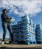  ??  ?? Volunteers load cases of water into vehicles in Flint.