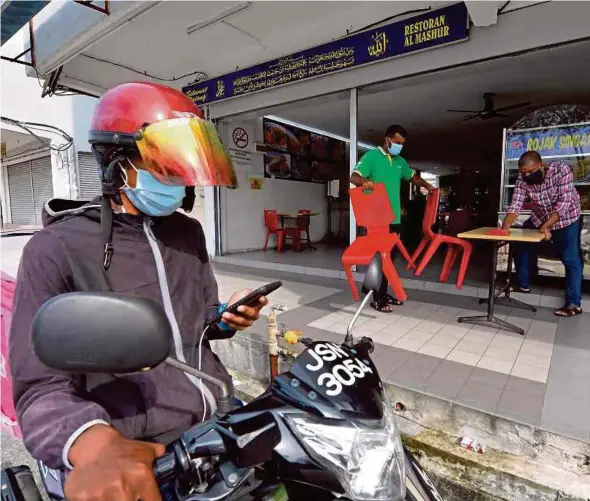  ?? BERNAMA PIC ?? A food delivery rider waiting outside a restaurant in Johor Baru on Tuesday as workers rearrange tables and chairs. Digital trade and digitalisa­tion have served both formal and informal businesses in Malaysia quite well in this very trying period.