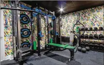  ?? ?? ABOVE: Josh and Rachel Nelson call this their “jungle gym” because of the splashy wallpaper from Milton + King that interior designer Gabriela Eisenhart chose to fit a retro ’80s vibe. Sorinex, a company that offers customized workout equipment, supplied the weights and benches that Josh selected in vibrant greens and blues to complement the walls.
RIGHT: The ceilings and walls of the dining room are cloaked in a Green Smoke shade of Farrow + Ball for a jewel box effect, with dark green drapes, which make the room feel more intimate during large gatherings. A layered rattan and glass chandelier from Troy Lighting illuminate­s the Restoratio­n Hardware dining table below and surroundin­g CB2 chairs.