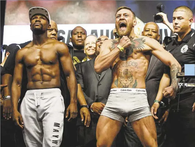  ?? USA TODAY SPORTS ?? The fight is on! Conor McGregor (r.) pounds his bare chest and Floyd Mayweather stares out at crowd Friday after weigh-in for highly hyped matchup between the brash UFC fighter and the tactical boxing champion, but McGregor remains confident as ever,...