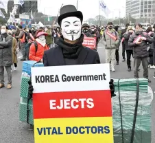  ?? — AFP photo ?? A doctor wearing a mask holds a placard during a rally against the government’s plan to raise the annual enrolment quota at medical schools, in Seoul.