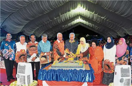  ??  ?? A show of unity: Najib and Juhar (on Najib’s left) together with their wives Datin Seri Rosmah Mansor and Puan Norlidah R.M. Jasni (in yellow headscarf) cutting the cake to mark the Malaysia Day celebratio­ns at the Likas Sports Complex in Kota...