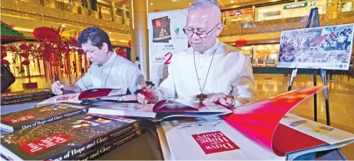  ?? SUNSTAR FOTO / AMPER CAMPAÑA ?? IEC BOOK.
Cebu Archbishop Jpse Palma (right) and Auxilliary Bishop Dennis Villarojo sign copies of the book Days of Hope and Glory, which is about the holding of the 51st Internatio­nal Eucharisti­c Congress in Cebu last year.