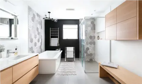  ??  ?? La toile de fond anthracite se marie à ravir à la céramique murale à motifs qui anime la pièce. Cette dernière affiche clairement ses tendances scandinave­s à travers le bois blond du meuble-lavabo, du banc et des rangements pratiques.