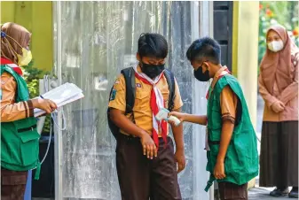  ?? DIPTA WAHYU/JAWA POS ?? PENGECEKAN: Sejumlah anggota satuan tugas Covid-19 sekolah memeriksa suhu tubuh siswa yang akan mengikuti pembelajar­an tatap muka di SDN Ketintang 1, Surabaya.