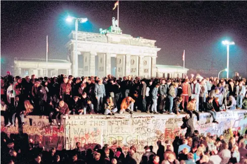  ??  ?? BREAKING DOWN BARRIERS: Thousands of young East Berliners crowd atop the Berlin Wall, near the Brandenbur­g Gate in 1989.