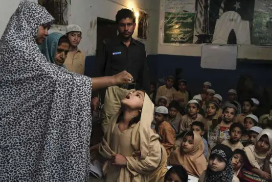  ?? FOTO: FAREED KHAN, AP/NTB SCANPIX ?? En pakistansk helsearbei­der gir poliovaksi­ne til en skolejente i Karachi i 2014. Stadige angrep mot helsearbei­dere bidro til at soldater måtte beskytte helsearbei­derne mens de gjorde jobben sin.