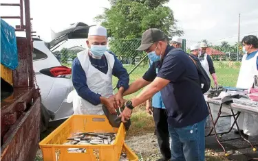  ??  ?? Moveable market: Syed Abu Hussin (left) unloading fish to be distribute­d through the mobile shop programme in Kamunting. — Bernama