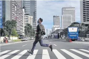  ?? BLOOMBERG ?? A commuter wearing a protective face crosses a street in the central business district in Jakarta, Indonesia. Asean needs to adapt to face challenges in the post-pandemic era.