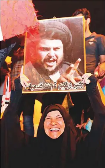  ?? AP ?? An Iraqi woman holds a picture of Moqtada Al Sadr as his followers celebrate election results in Tahrir Square, Baghdad.