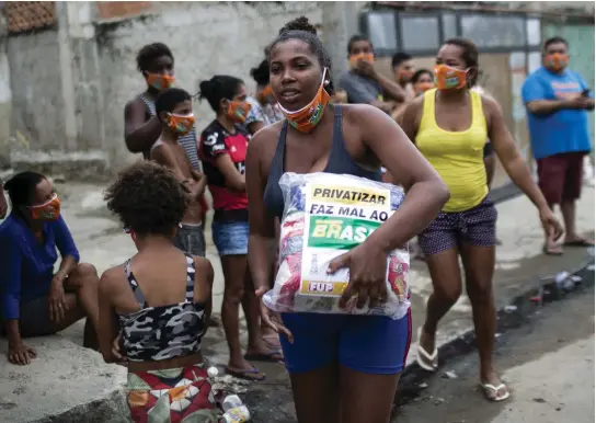  ?? FOTO: BRUNA PRADO/TT-AP ?? Caroline Rocha i Rio de Janeiro, Brasilien, bär på en påse med donerade livsmedel. Jobben har minskat under coronakris­en och lönerna likaså. Familjen Rocha lever på makens barberarlö­n – att inte jobba är inget alternativ för den som är fattig, pandemin till trots, konstatera­r hon.