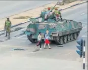  ?? AFP ?? Young women walk past an armoured vehicle stationed by an intersecti­on as Zimbabwe soldiers regulate traffic in Harare.