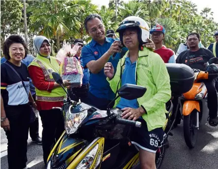  ??  ?? Hasni helping to put on a motorcycli­st’s helmet during a road safety campaign in Johor Baru on Feb 12.