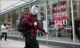  ?? STEVEN SENNE — THE ASSOCIATED PRESS ?? A passer-by walks past a store closing sign, right, in the window of a department store on Tuesday in Boston.