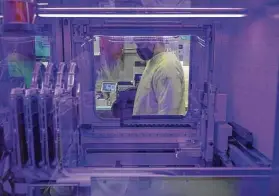  ?? Ted S. Warren / Associated Press ?? Steven Grimmett, a microbiolo­gist on the COVID-19 team at the Washington State Department of Health’s Public Health Laboratory, is seen through a window of a machine that identifies positive and negative cases on Dec. 7 in Shoreline, Wash.