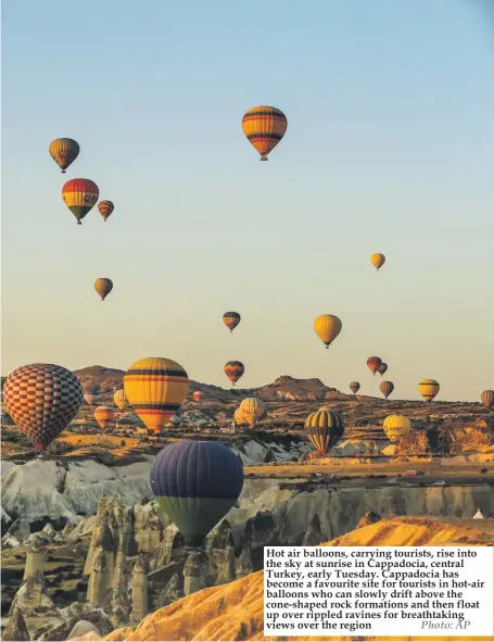  ??  ?? Hot air balloons, carrying tourists, rise into the sky at sunrise in Cappadocia, central Turkey, early Tuesday. Cappadocia has become a favourite site for tourists in hot-air balloons who can slowly drift above the cone-shaped rock formations and then...