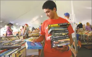  ?? Erik Trautmann / Hearst Connecticu­t Media ?? Bridgeport resident Alexis Ramirez grabs a little bit of everything while shopping at the Pequot Library’s Summer Book Sale in the Southport section of Fairfield on Friday. The book sale runs through Tuesday, and benefits library programs.