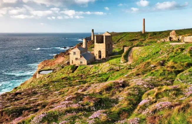  ??  ?? Levant Mine cooling pool, boiler house, with its chimney, and whim building next to it, and the taller pump engine house to the right. Pendeen Lighthouse can just be seen off the coastline.