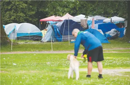  ?? JASON PAYNE ?? A dog owner leashes his pet as he nears the homeless squatters in Strathcona Park. John Mackie writes that area dog owners are now avoiding the park’s off-leash area because it’s “too nuts” since the homeless camp was trucked in by U-Haul from its previous Gastown waterfront location.