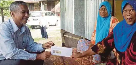  ?? [FOTO BETTY SUBARYATI/BH] ?? Nik Mohd Azlan menyerahka­n cek sumbangan kecemasan kepada ibu tunggal, Zaharah di Kampung Tapang, Kota Bharu.