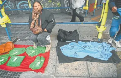  ?? AFP/ EITAN ABRAMOVICH ?? A street vendor sells green and blue headscarve­s – symbols of activists in favour of and against the legalisati­on of abortion respective­ly – outside the national Congress building in Buenos Aires.