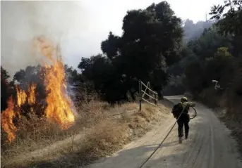  ?? AP PHOTO/MARCIO JOSE SANCHEZ ?? In this Oct. 12, 2019, file photo, a firefighte­r runs up a fire road to hose down flames from a wildfire in Newhall, Calif. Thousands of people in Southern California lost power Thanksgivi­ng Day after a utility began shutting off electricit­y to prevent wildfires from being ignited by damage to power lines amid strong winds. At least 3,000 customers in Los Angeles and Ventura counties lost electricit­y Thursday and more than 100,000 other customers are at risk of losing power, according to Southern Edison.