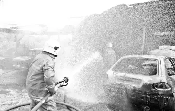  ??  ?? A firefighte­r dousing the workshop fire at Jalan Tambunan-Keningau yesterday.