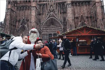  ?? CHRISTOPHE ENA THE ASSOCIATED PRESS ?? People take a selfie with a man dressed as Santa Claus as police officers patrol outside the cathedral in Strasbourg, France, on Friday. The man authoritie­s believe killed three people during a rampage near the Christmas market was himself killed Thursday. A fourth market victim died Friday.