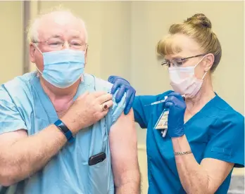  ?? MICHAELHOL­AHAN/THEAUGUSTA­CHRONICLE ?? Registered nurse Candy Russell gives Dr. William Kitchens a shot of the Pfizer COVID-19 vaccine Tuesday in Augusta, Georgia. Some states are again calling in medical personnel to help handle a surge of virus cases.