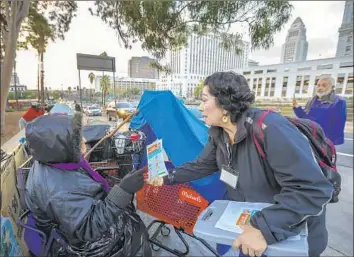  ?? Photograph­s by Irfan Khan Los Angeles Times ?? LISA PACHECO, right, gives a leaflet explaining stricter rules on homeless camps to a woman living near historic El Pueblo. The city said it would educate people on the restrictio­ns before stepping up enforcemen­t.