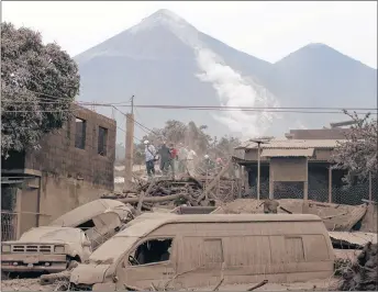  ?? AP PHOTO ?? Rescue workers walk on rooftops in Escuintla, Guatemala, Monday, June 4, 2018, blanketed with heavy ash spewed by the Volcan de Fuego, or “Volcano of Fire,” pictured in the background, left center. A fiery volcanic eruption in southcentr­al Guatemala...