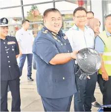  ?? ?? Norizan shows a half-shell helmet, brought in by a motorcycli­st to be exchanged with a Sirim-approved one, during the road safety campaign at the Petronas Jalan Lanang Barat station.