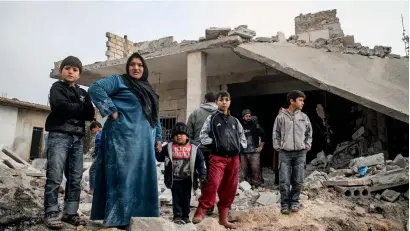  ?? AFP ?? Syrians stand in a street next to debris and rubble from buildings which were damaged by reported air strikes in the rebel-held town of orum Al Kubra, in the northern Syrian province of Aleppo, on Saturday. —