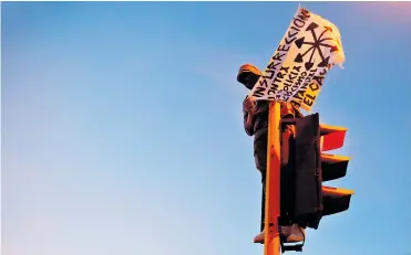 ?? EFE Y MINDEFENSA ?? Un manifestan­te exhibe una pancarta desde un semáforo en Cali durante la protesta del pasado lunes.