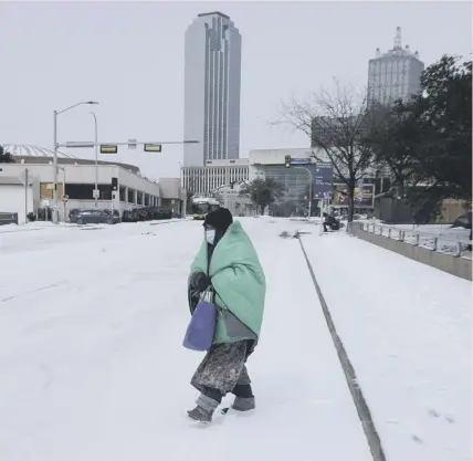  ??  ?? 0 A woman wrapped in a blanket crosses a frozen street near downtown Dallas in Texas