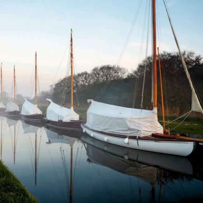  ??  ?? Mist bathes a neat line of moored sailboats on the glass-like surface of the water at Horsey Staithe on a still January morning.