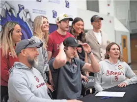  ?? DOUG HOKE/THE OKLAHOMAN ?? Bethany football standout Taylor Heim celebrates after signing his national letter of intent with the Sooners by putting an OU hat while surrounded by family and friends Friday afternoon in Bethany.
