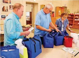  ??  ?? Lee Mullican, Roger Laubhan and Burchie Smith pack up meals to be delivered.