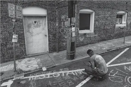  ?? Associated Press ?? ■ Ahmed Mohamed writes a message Saturday in the alleyway where Heather Heyer was killed during last year’s Unite the Right rally in Charlottes­ville, Va.