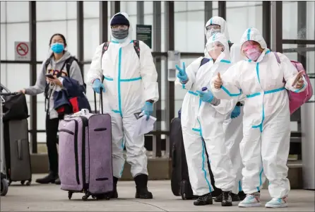  ?? The Canadian Press ?? People wearing protective face masks, goggles and Tyvek suits — and who said they travelled from Colombia — gesture while waiting for a shuttle at Vancouver Internatio­nal Airport in Richmond on Thursday.