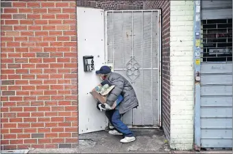  ?? [JOHN MINCHILLO/ THE ASSOCIATED PRESS] ?? Francisco Ramírez peers through a hole in a fence while looking for an address to deliver a box of groceries to a man in need April 18 in Queens, N,Y..