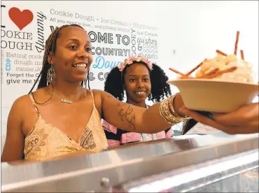  ?? DAN HONDA — STAFF PHOTOS ?? Angelyse Gray is handed her order as her daughter Azra watches Wednesday at the Cookie Dough Parlor in Pinole. The newly opened business serves ice cream and cookie dough, with a variety of toppings.