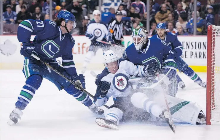  ?? — CP ?? Vancouver Canucks defenceman Ben Hutton, left, watches as Winnipeg Jets forward Patrik Laine slides into goaltender Jacob Markstrom Tuesday at Rogers Arena.